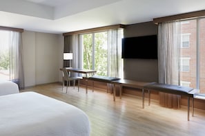 A hotel room with a large bed, a desk with a chair, a bench, and a TV mounted on the wall.