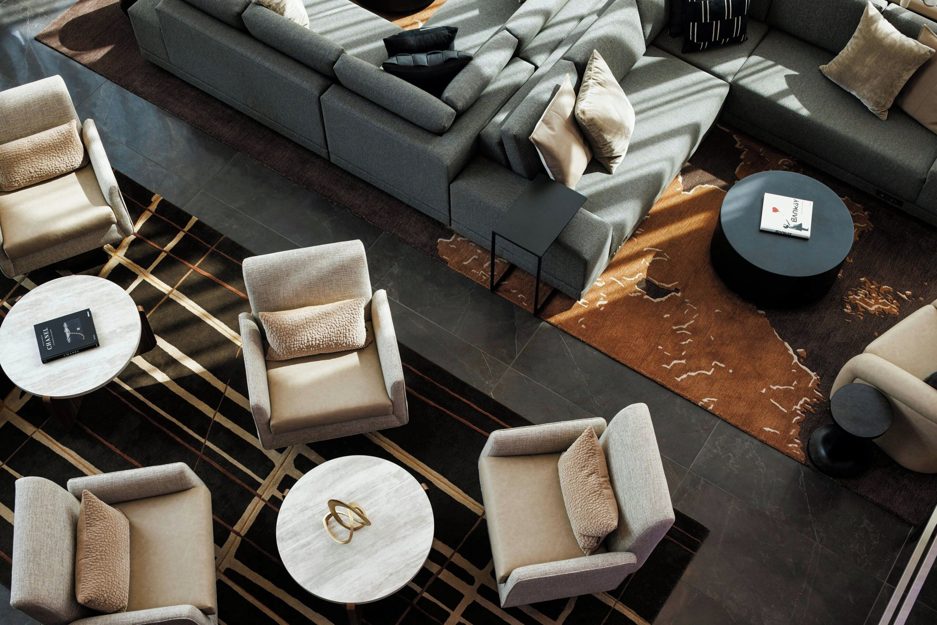 A modern lounge area with sofas, armchairs, and round tables, featuring a geometric patterned rug and a minimalist design.