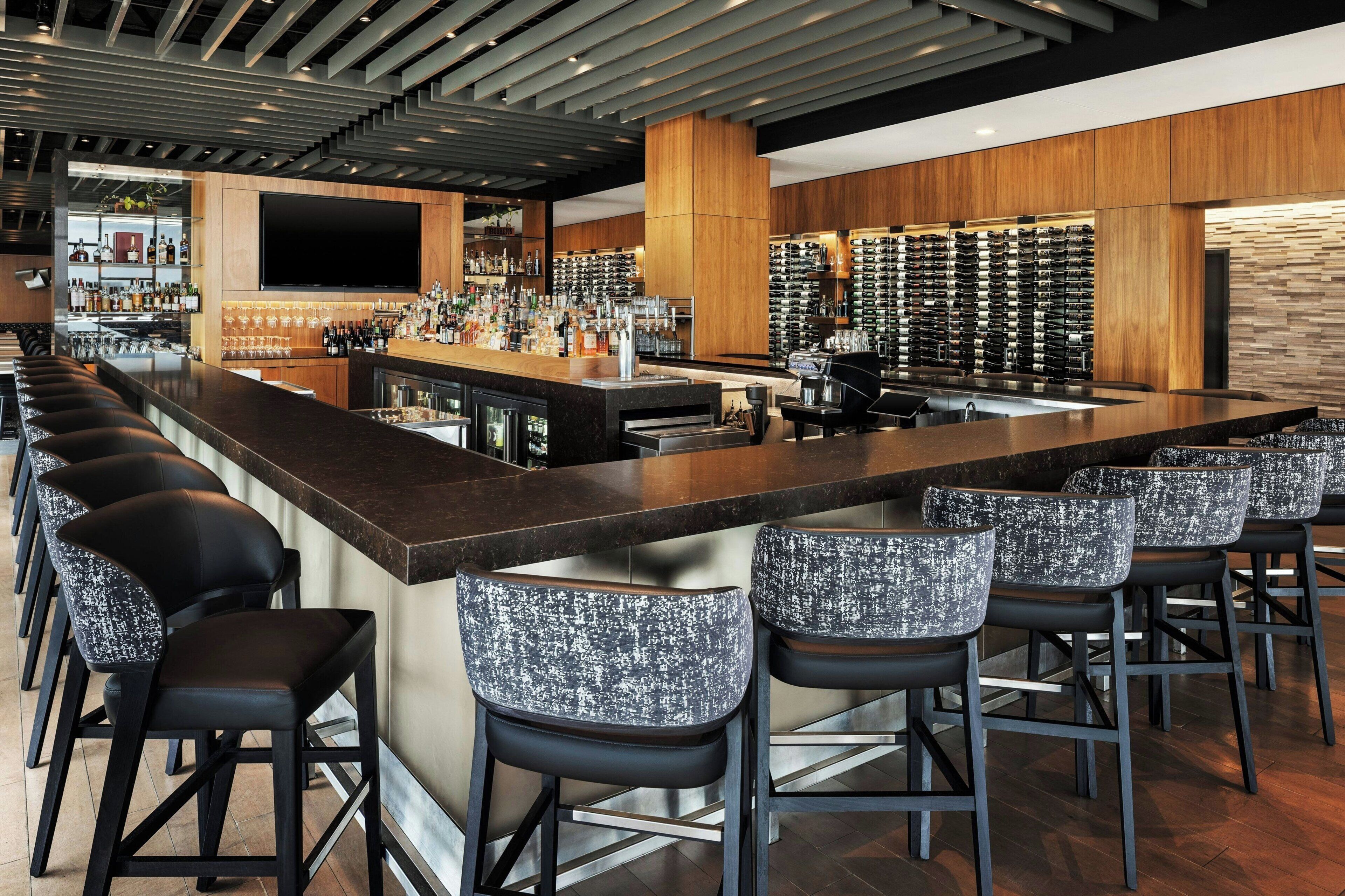 A bar area with a long counter, multiple stools, and a wall of wine bottles.