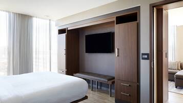 Una habitación de hotel con una cama grande, una banca, un armario y un televisor.