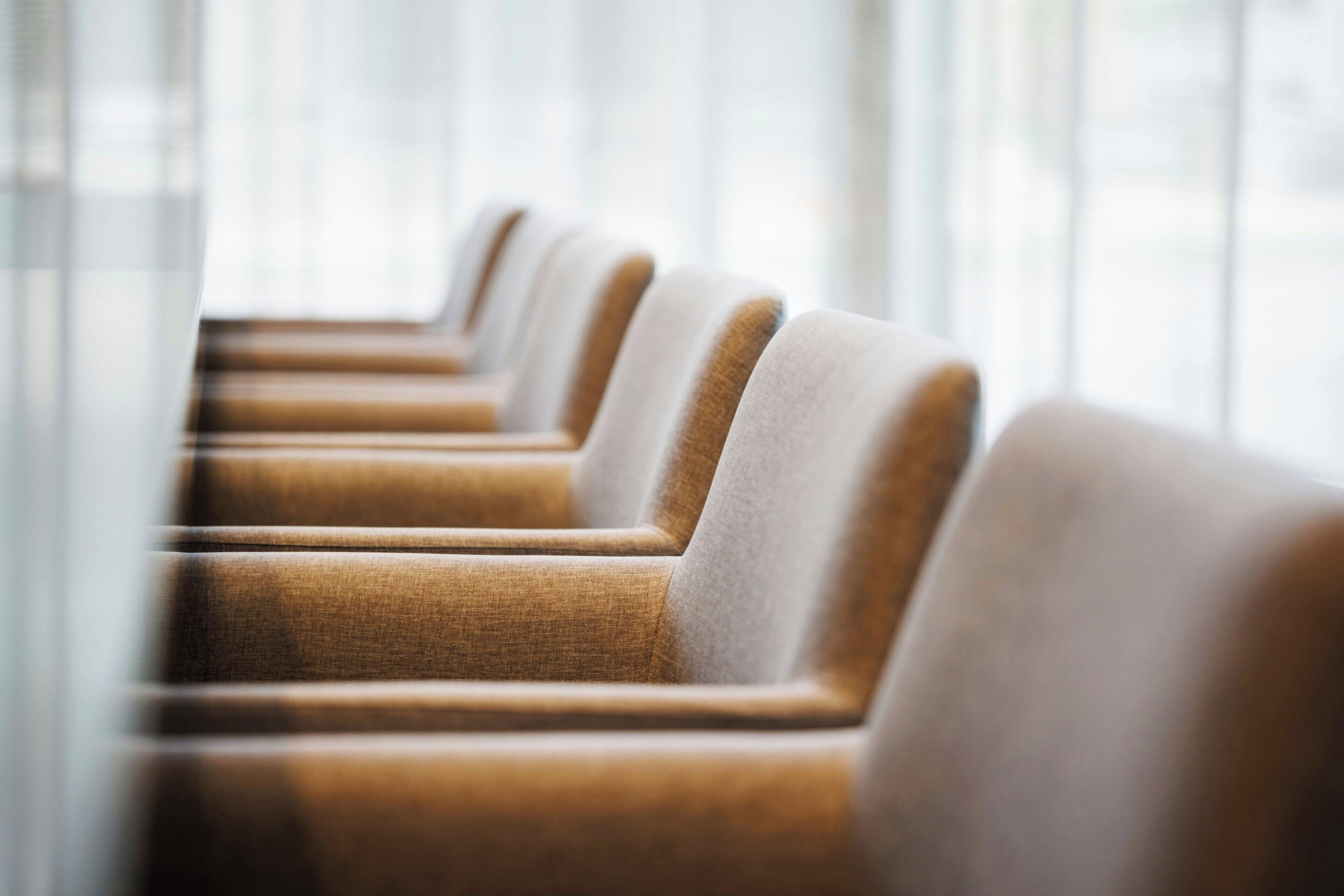 A row of chairs with a light brown fabric and a darker brown cushion, arranged in a row.