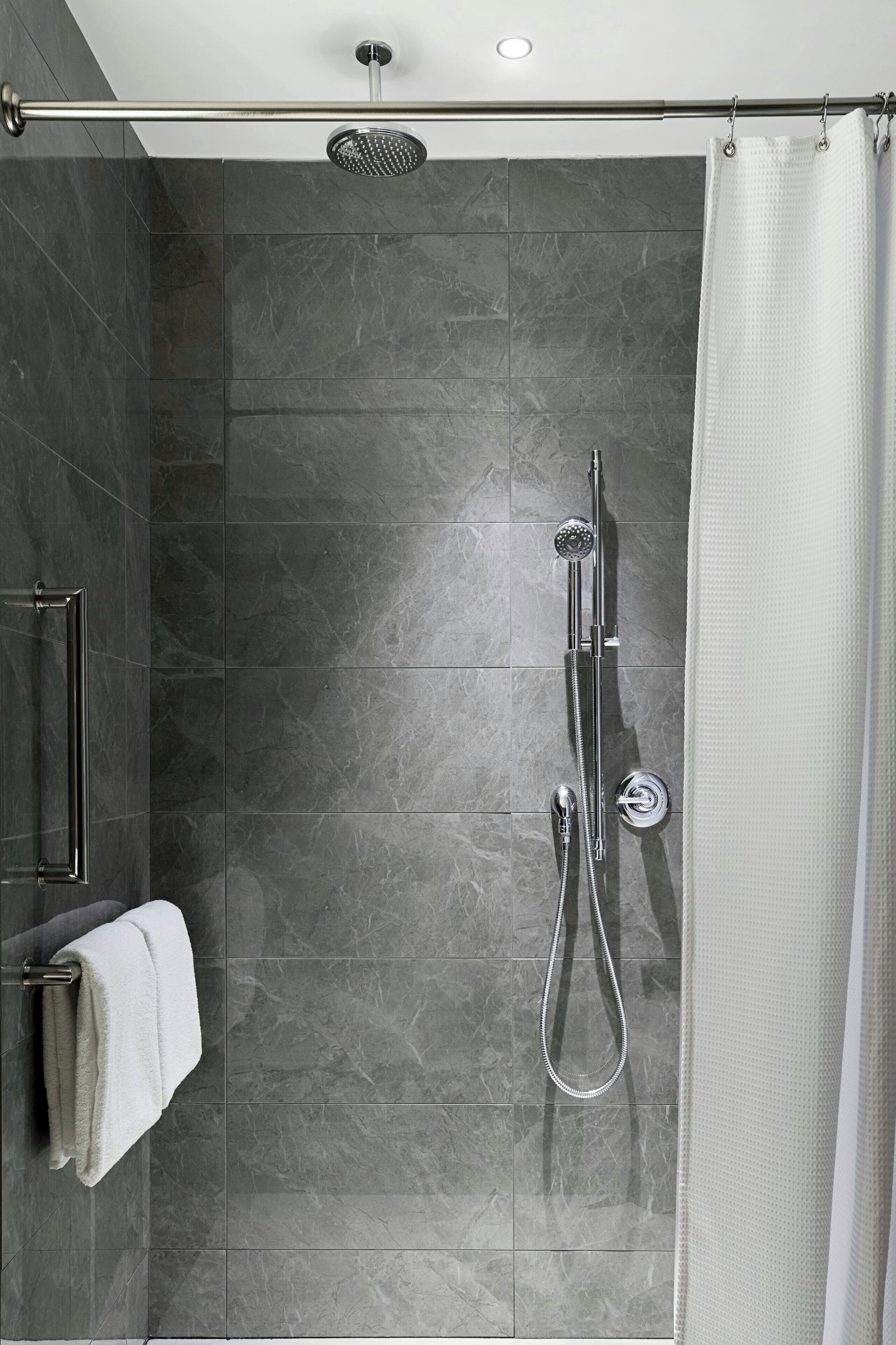 Une douche moderne dotée d’un pommeau de douche à effet pluie, d’un pommeau de douche à main et d’un flexible de douche à main.