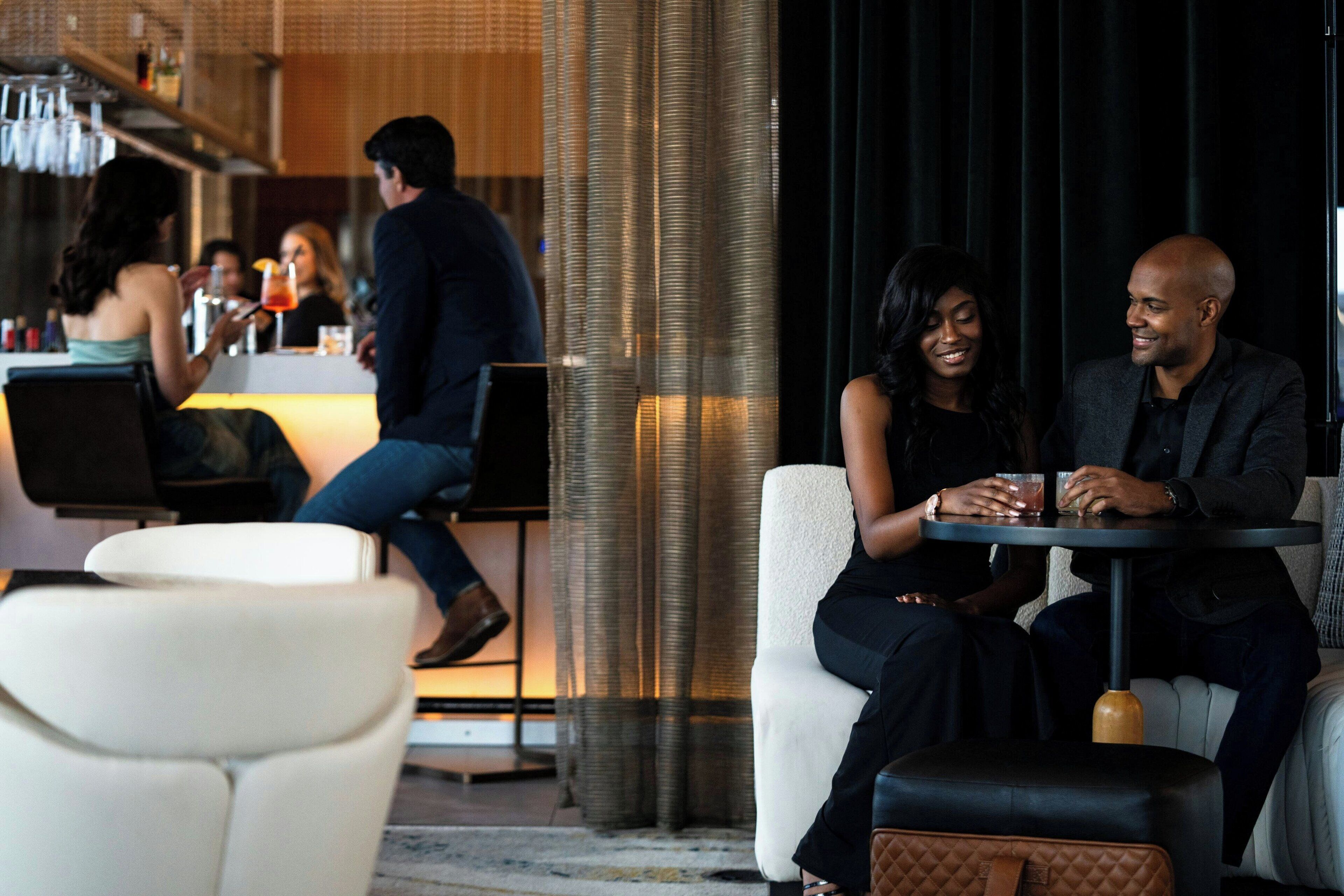 A modern bar area with seating. There are bar stools and a high bar with bottles.