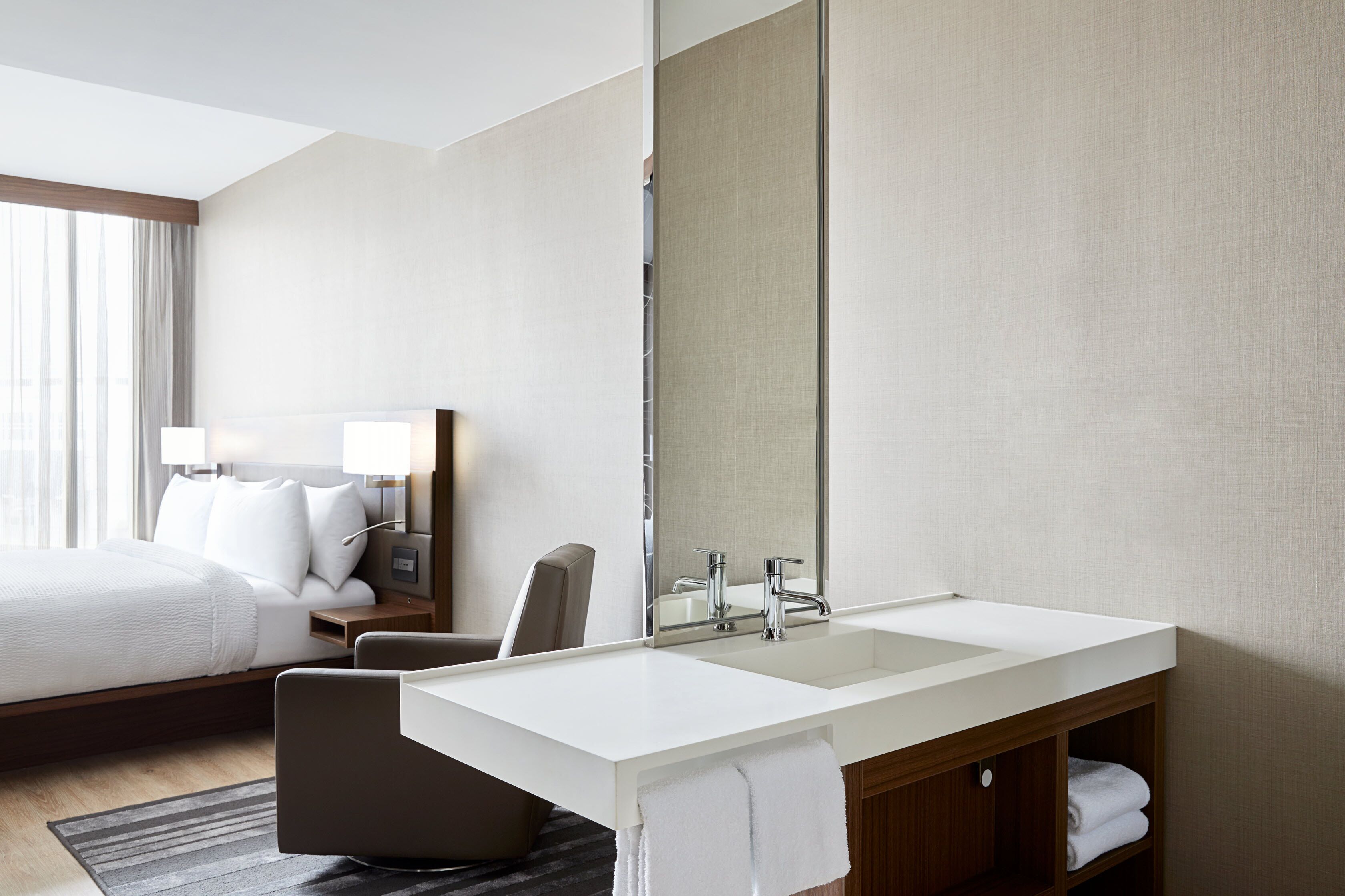 A hotel room with a large bed, a sitting area, a double sink vanity, and a large mirror.