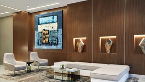 A modern living room with a large abstract painting, two armchairs, a glass coffee table, and a white sofa. - AC Hotel Raleigh North Hills (Raleigh)