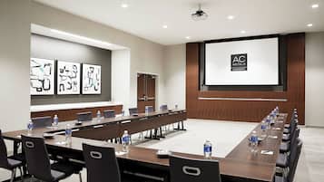 A conference room with a long table, chairs, and a projector screen displaying the AC Hotels logo.