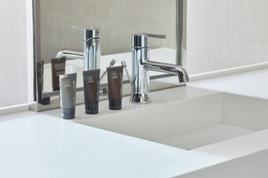 Un baño moderno con un grifo cromado, un espejo y tres productos para el cuidado de la piel sobre el lavamanos.