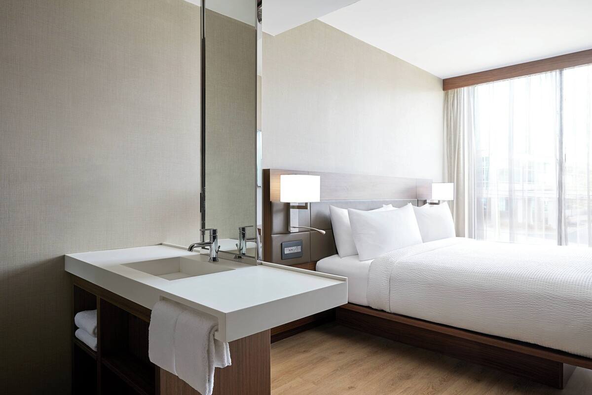 A hotel room with a large bed, a white bathroom sink, and a mirror.