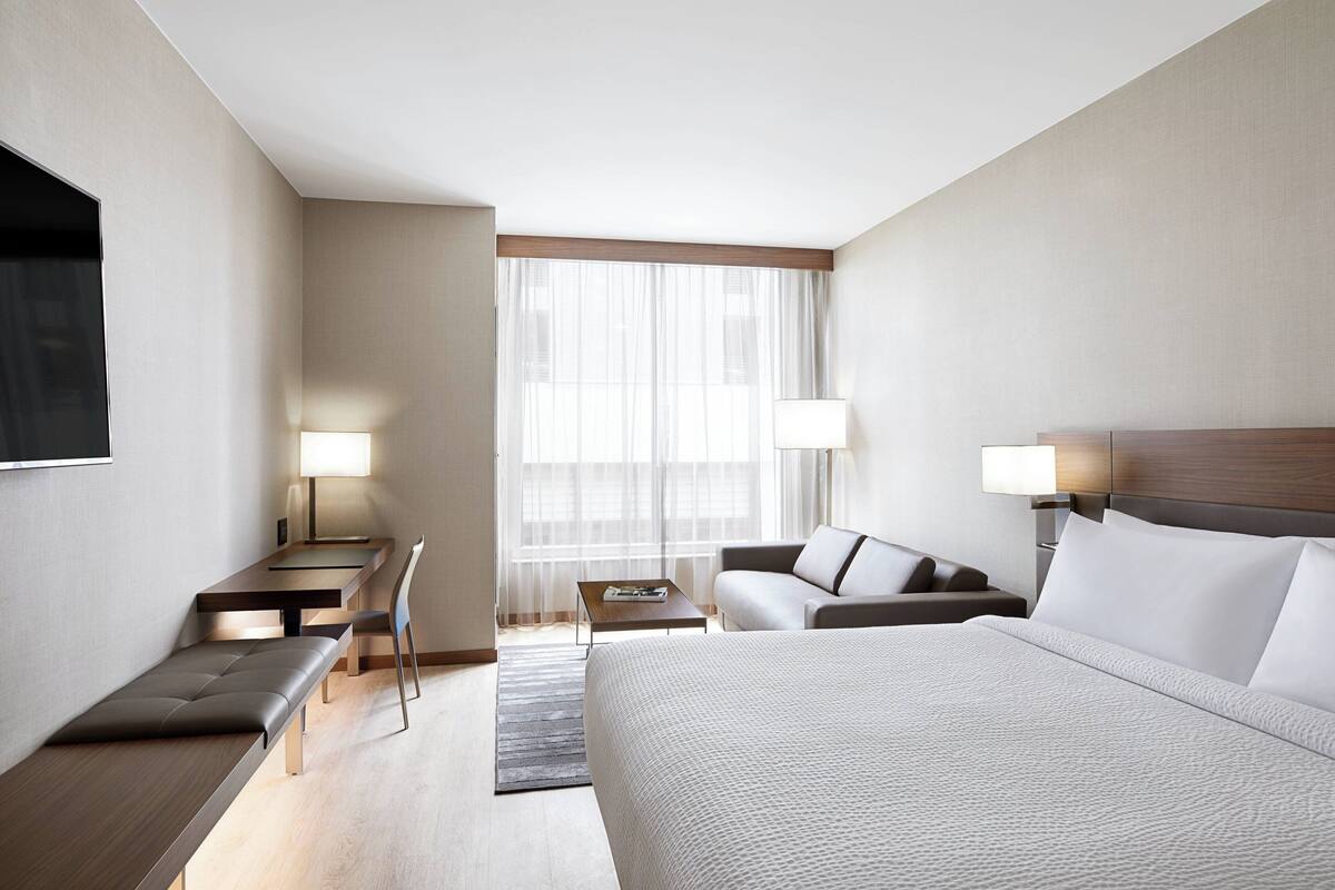 A hotel room with a large bed, a desk, a chair, a sofa, and a TV.