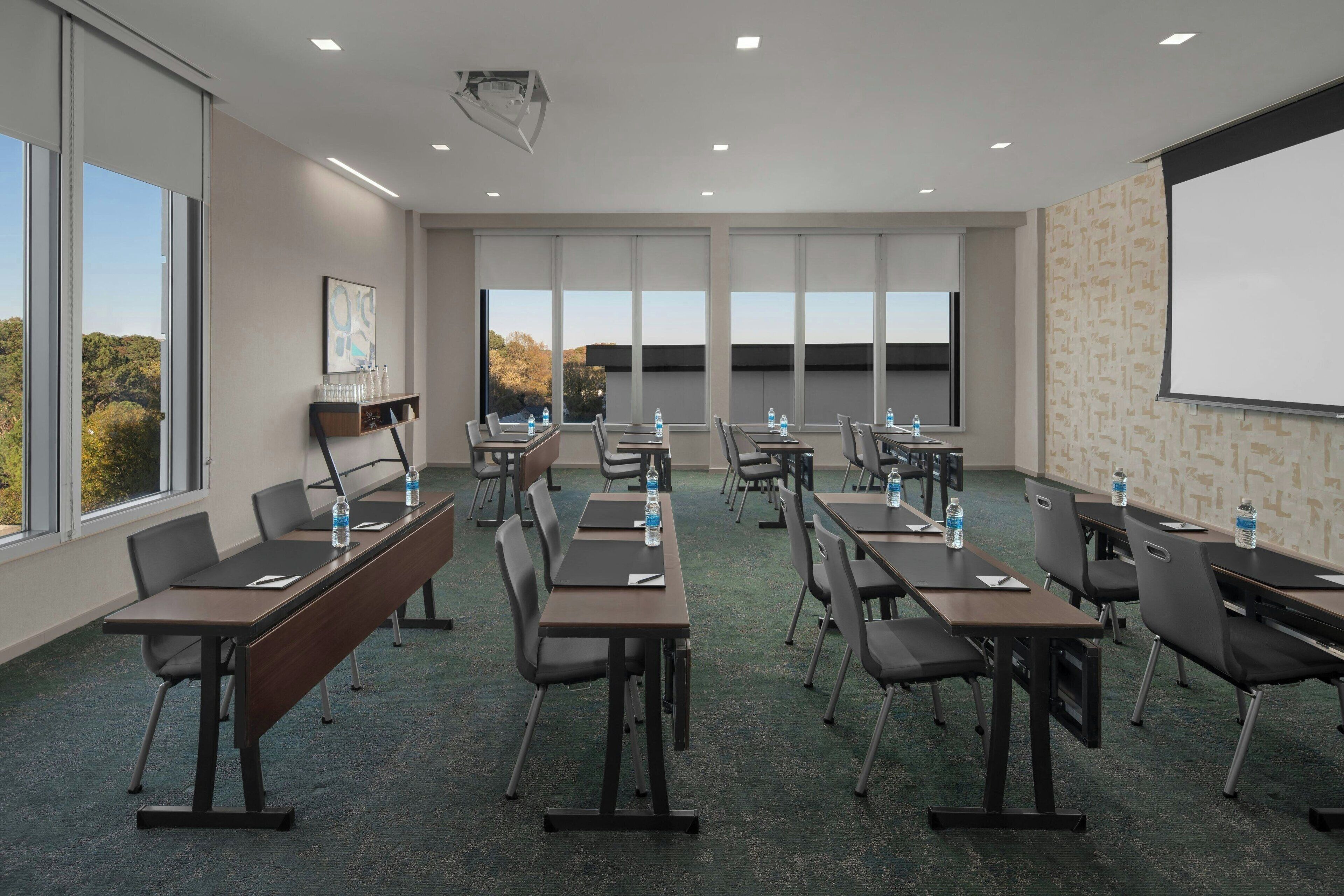 A conference room with tables, chairs, and a projector screen.