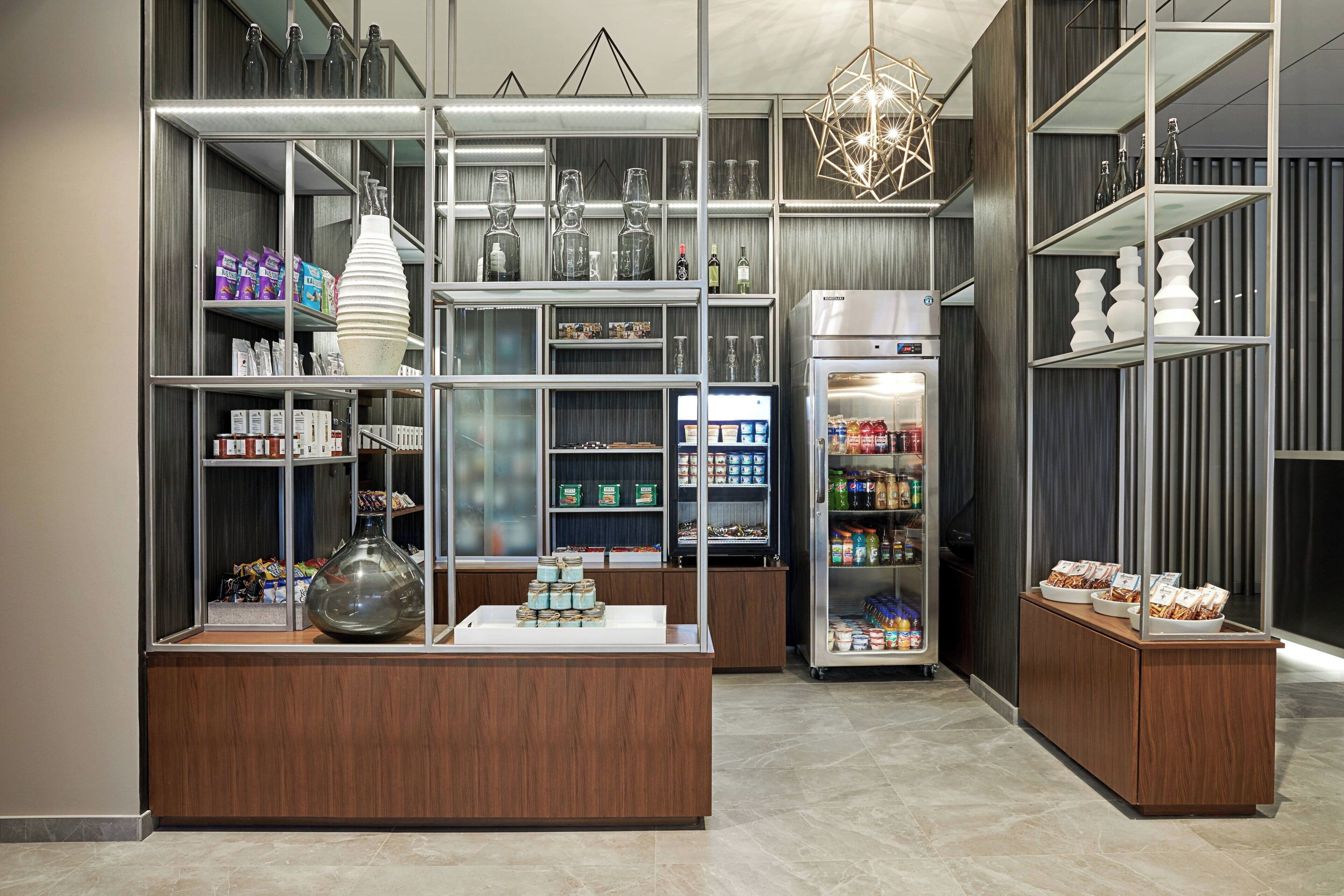 A modern hotel lobby with a central reception desk, glass display cases, and a refrigerated display.
