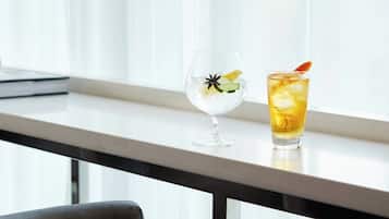 Two glasses of beverages on a table near a window with sheer curtains.