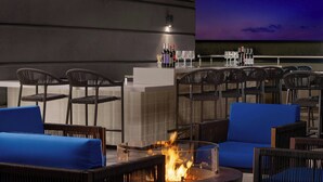 An outdoor seating area with wicker chairs and a central fire feature. - AC Hotel Raleigh North Hills (Raleigh)