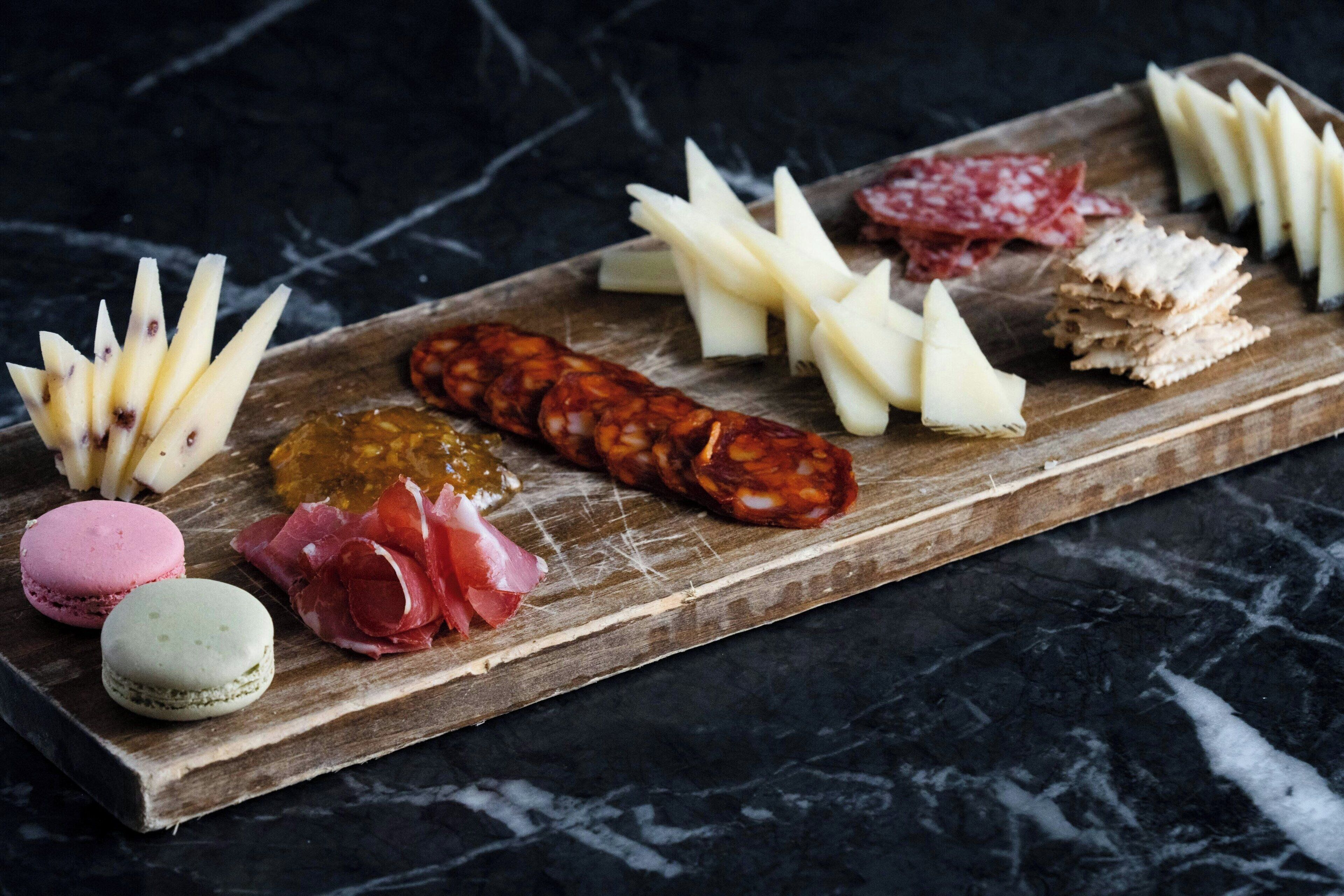 A wooden board with various cheeses, cured meats, and macarons.