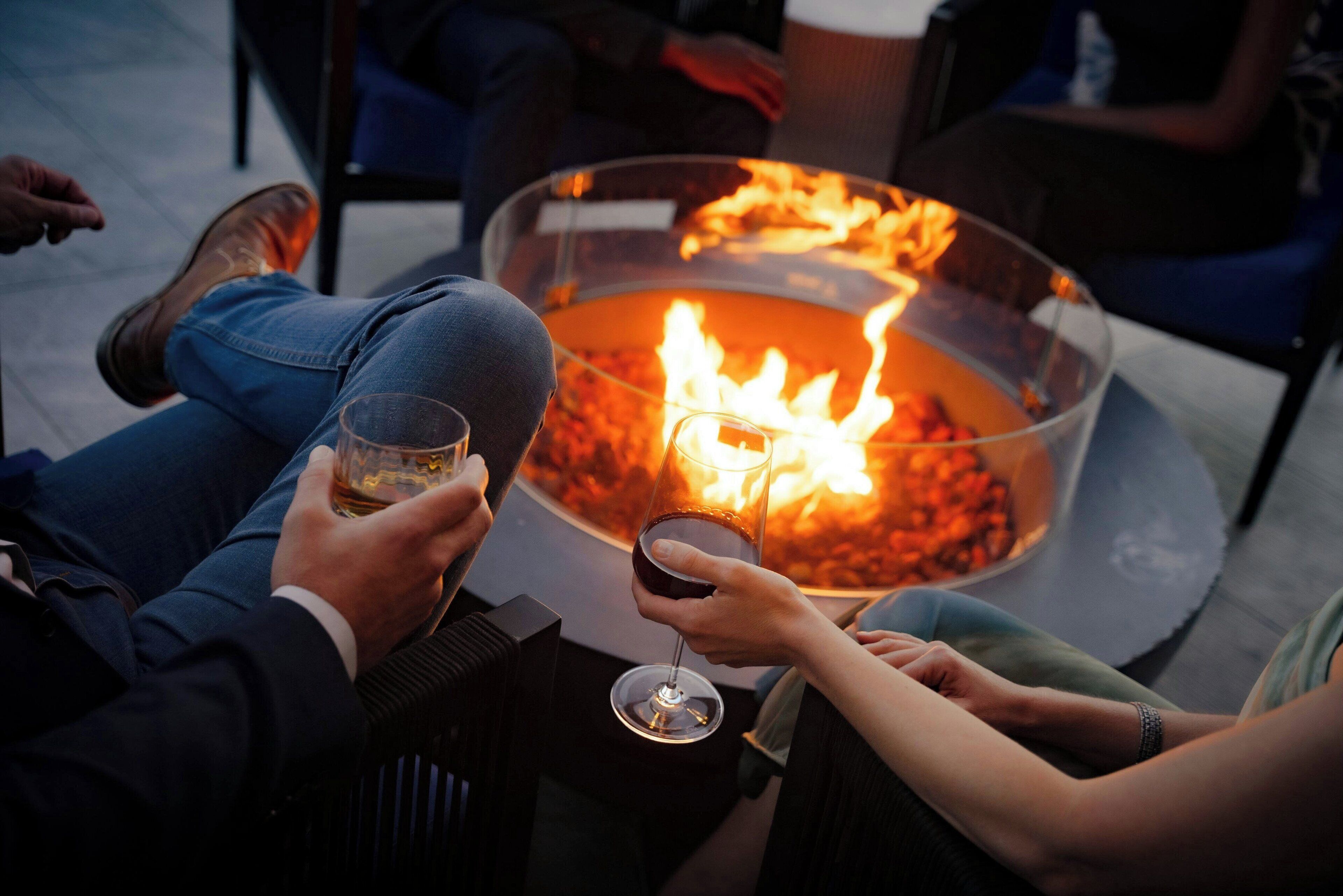 People sitting around a fire pit with glasses of wine.