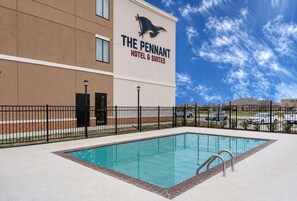 A hotel with a swimming pool, a fenced area, and a clear sky.