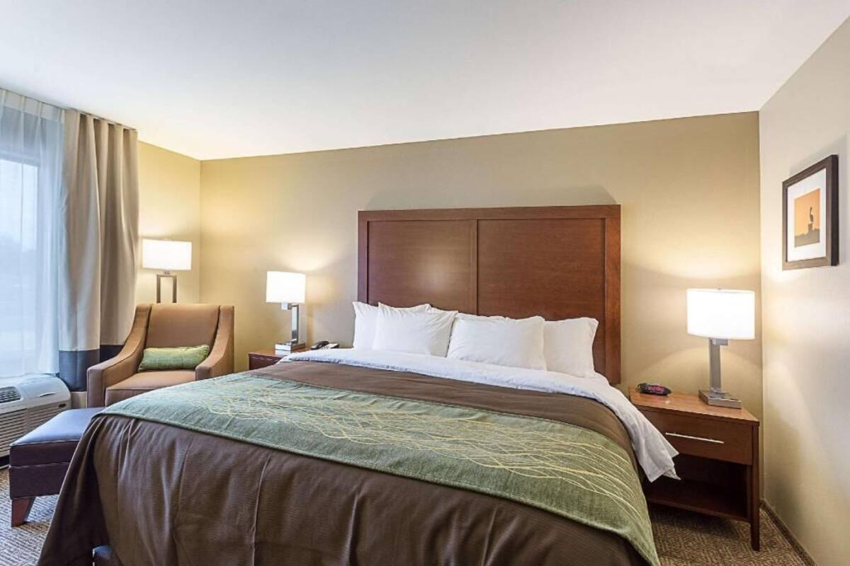 A hotel room with a large bed, two bedside tables with lamps, a chair, and a window with curtains.
