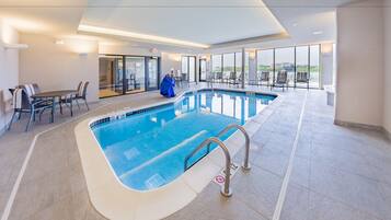 Ein Innenpool mit klarem Wasser, umgeben von Liegestühlen und einem Tisch.