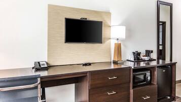 Une chambre d’hôtel avec un bureau en bois foncé, un téléviseur à écran plat fixé au mur, une lampe, une machine à café, un four à micro-ondes et un réfrigérateur.