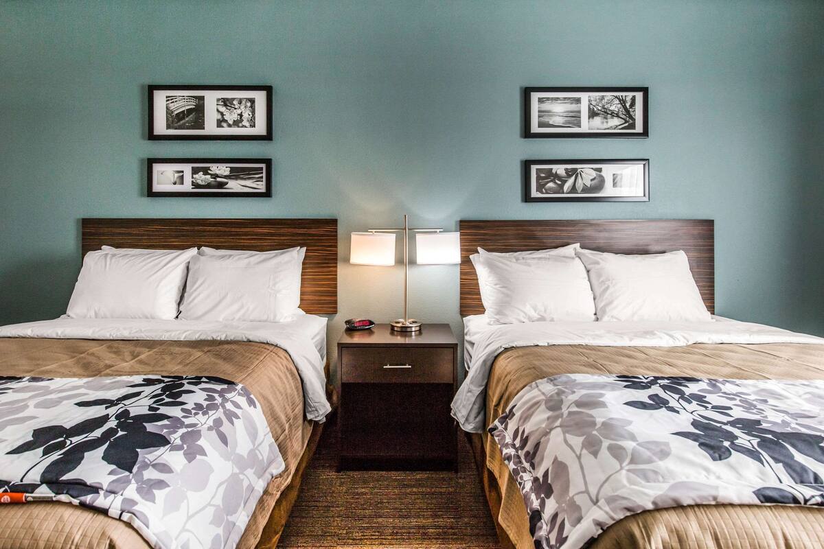A hotel room with two beds, a nightstand with a lamp, and framed pictures on the wall.