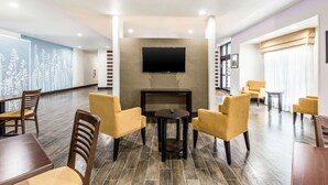 Un moderno hall de hotel con una televisión de pantalla plana montada en la pared, una chimenea y zonas de estar cómodas con sillas amarillas y mesas de madera.