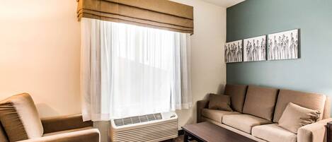 A living room with a beige sofa, a wooden coffee table, and a window with sheer curtains.