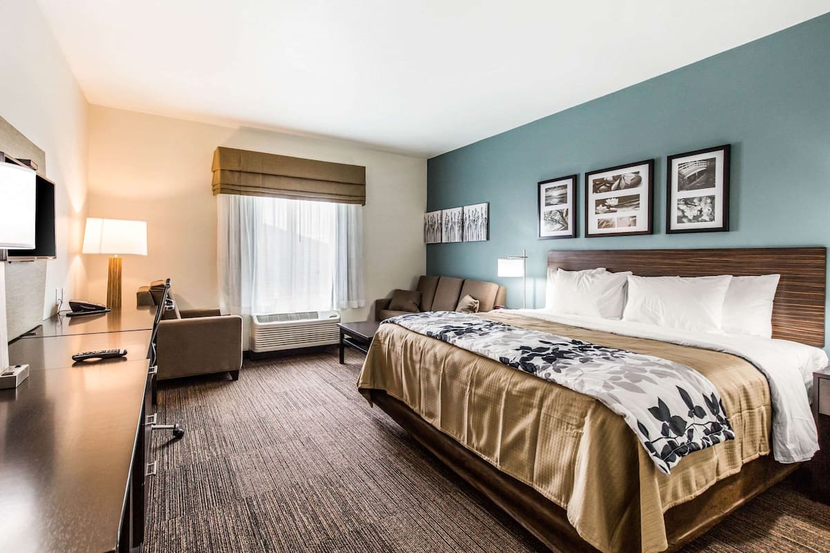 A hotel room with a large bed, a desk with a lamp, a chair, and a window with curtains.