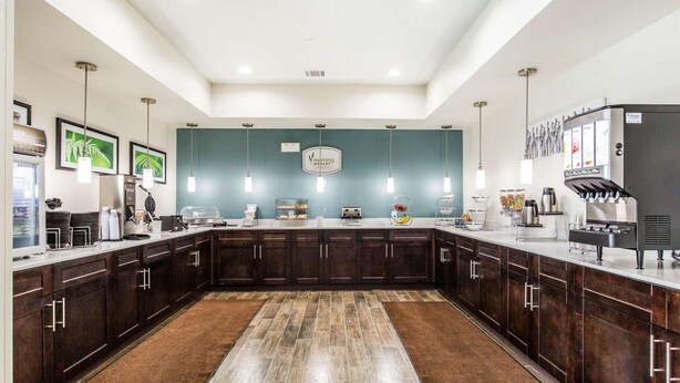 Una cocina moderna con armarios de madera oscura, encimera de mármol y una isla central. Se observan diversos electrodomésticos y una cafetera en la encimera.