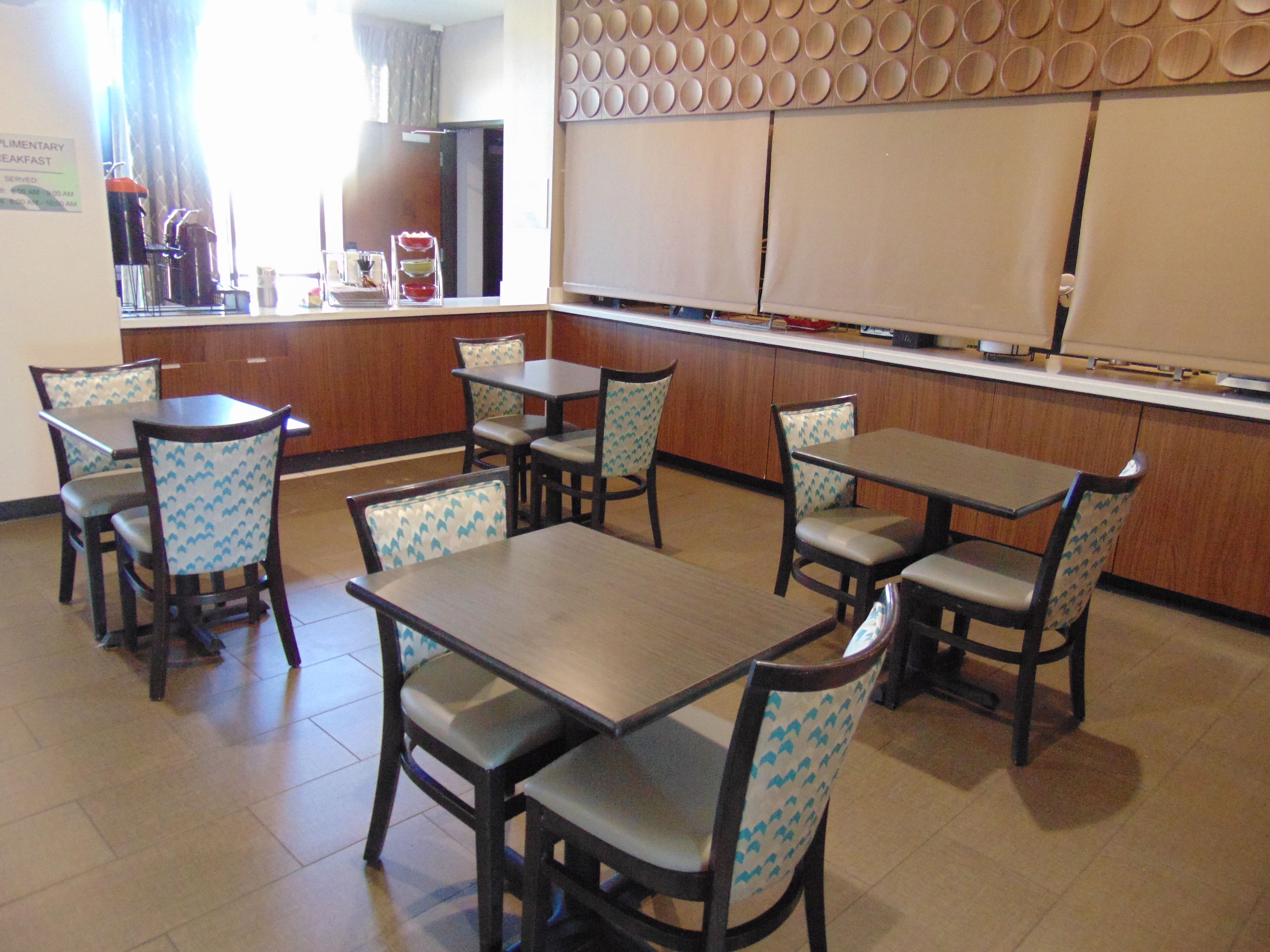 Un restaurante con mesas y sillas de madera, una zona de cocina y un letrero que anuncia desayuno.