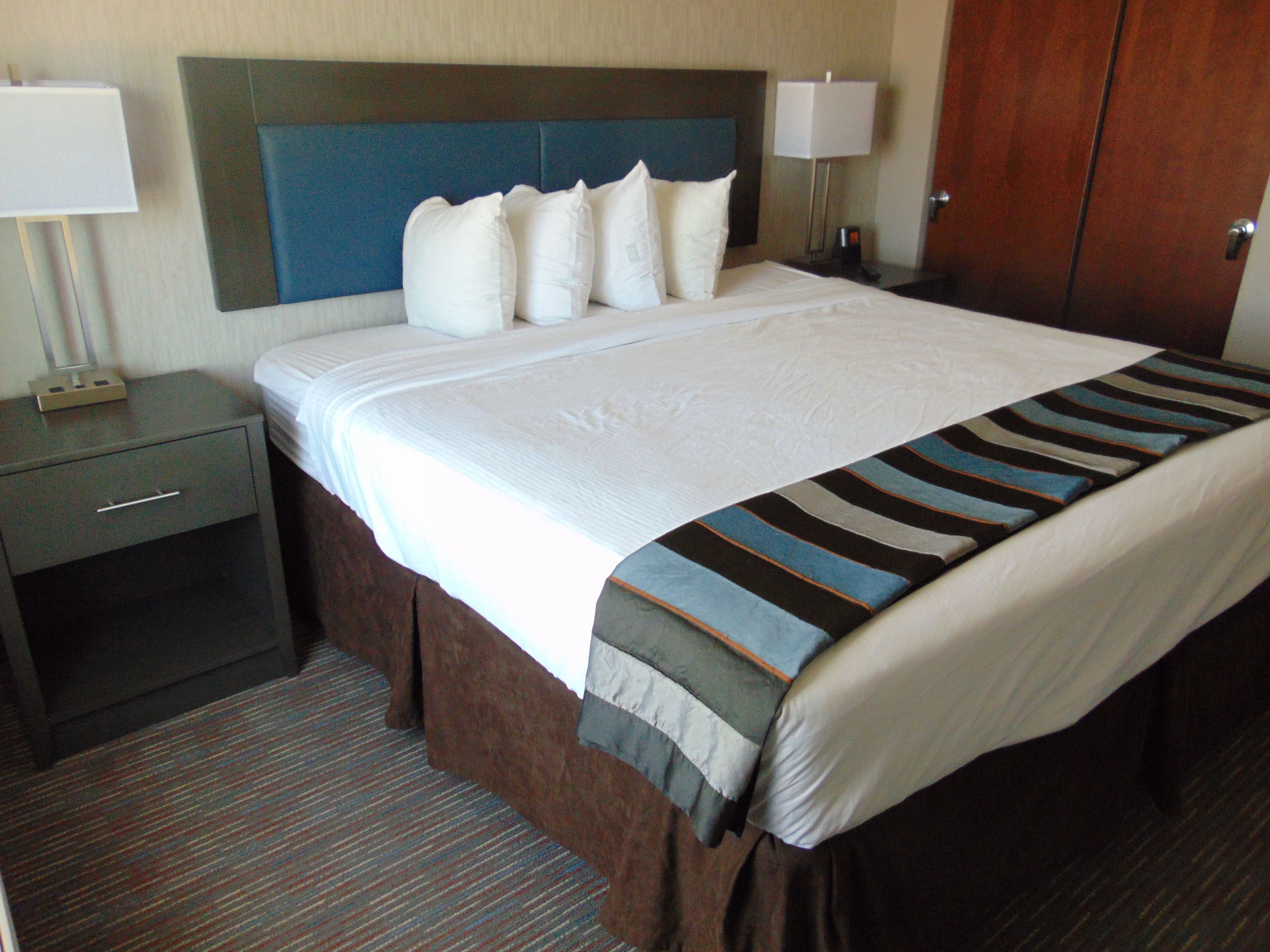 A hotel room with a large bed, a nightstand with a lamp, and a wardrobe.