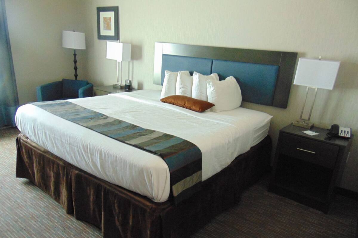 A hotel room with a large bed, a nightstand, a chair, and a desk with a lamp.