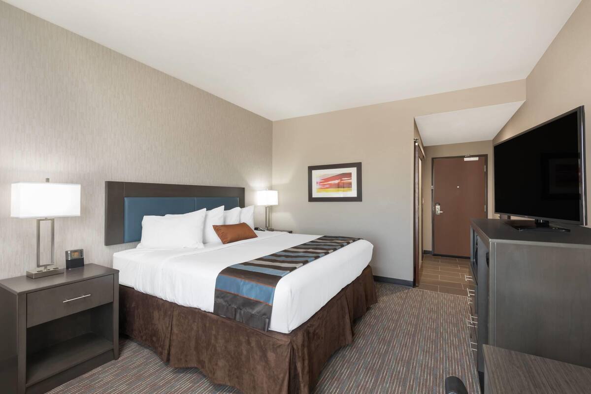 A hotel room with a bed, bedside tables, a TV, and a door.