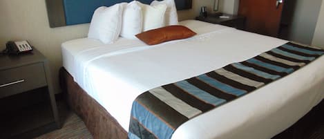 A hotel room with a large bed, a nightstand with a phone, a lamp, and a door.
