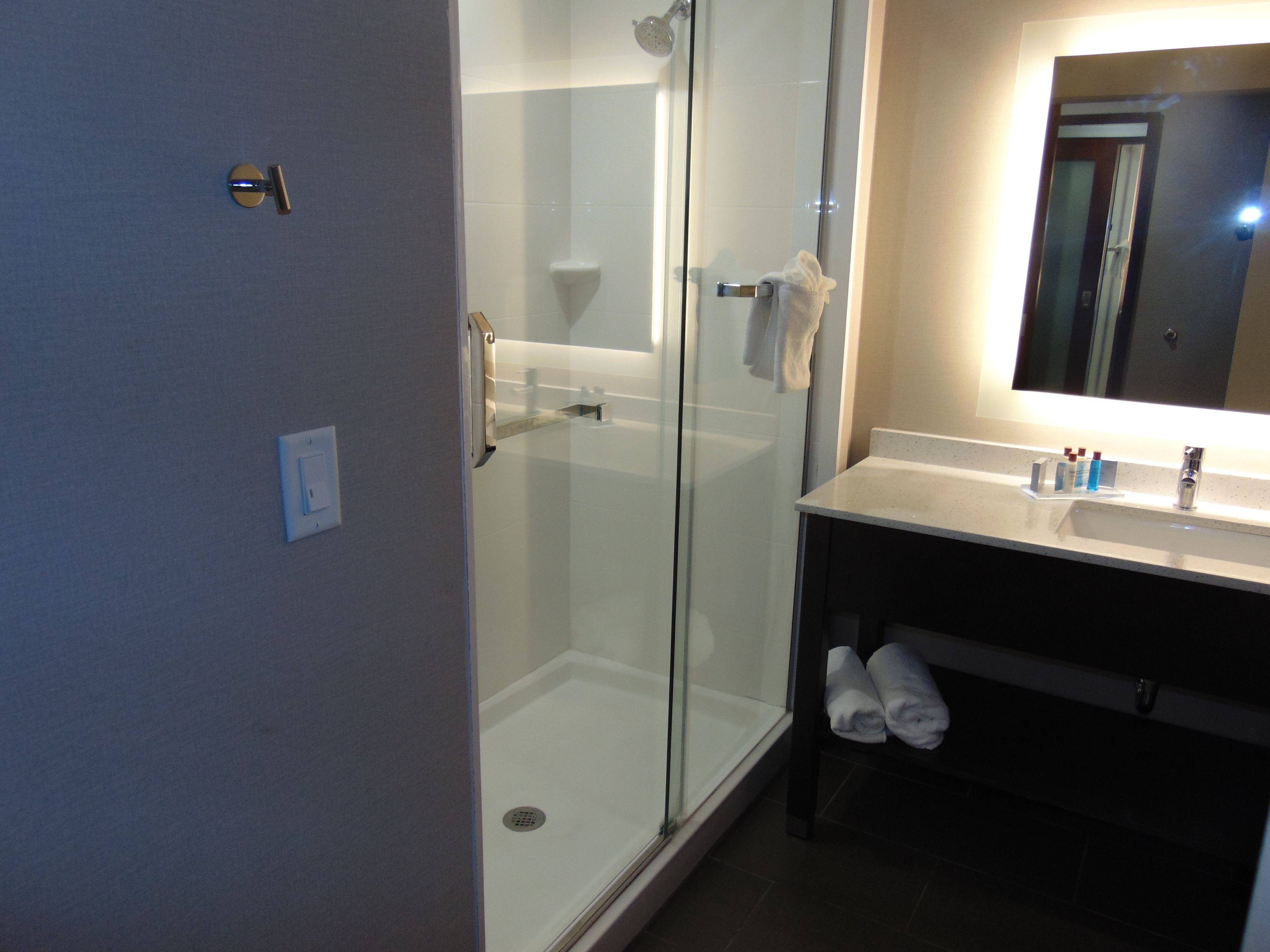 Un baño moderno con ducha envuelta en vidrio, un lavabo blanco con espejo y un perchero con toallas.