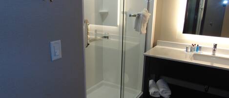 Un baño moderno con ducha envuelta en vidrio, un lavabo blanco con espejo y un perchero con toallas.