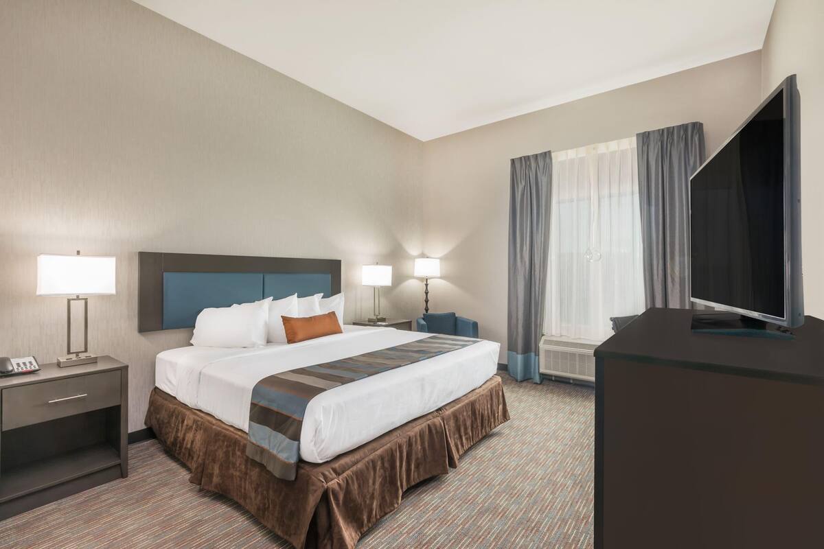 A hotel room with a bed, bedside tables, lamps, a flat-screen TV, and a large window with curtains.