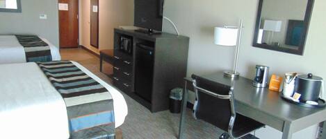 Habitación de hotel con cama, escritorio, silla, cómoda, televisor, lámpara y espejo.
