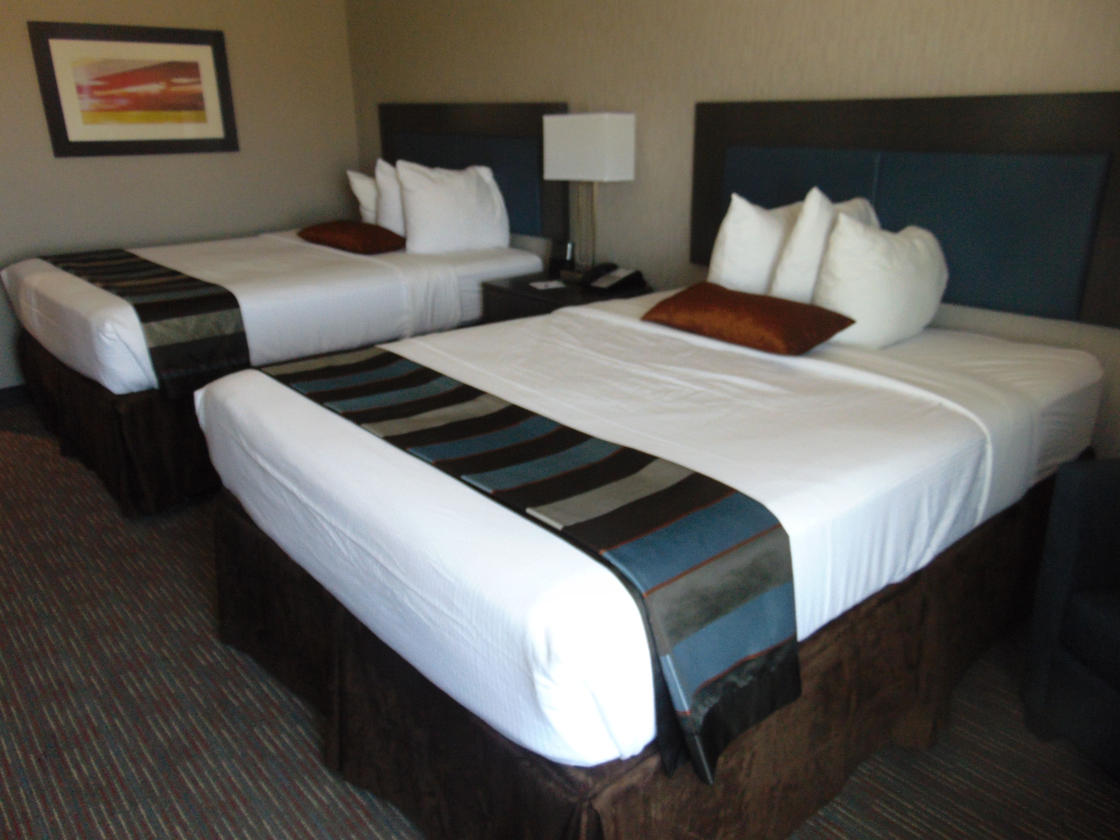 A hotel room with two beds, a nightstand, and a lamp.