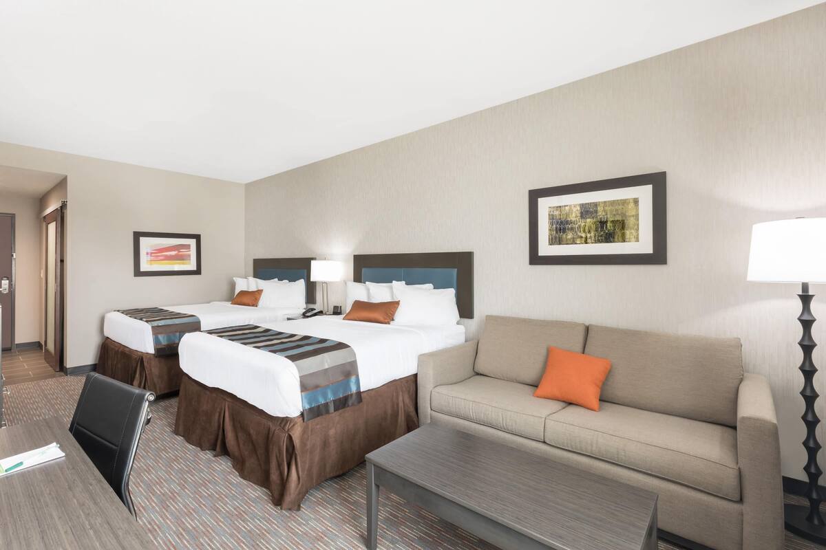A hotel room with two beds, a sofa, a coffee table, and a desk.