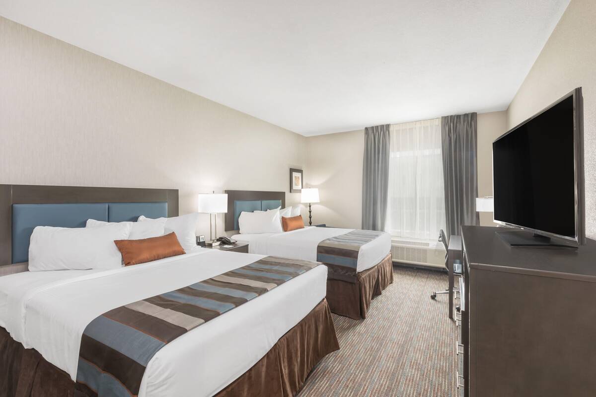 A hotel room with two beds, a flat-screen TV, a desk, and a window with curtains.