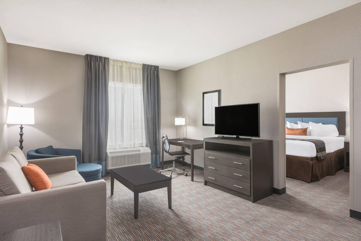 A hotel room with a sofa, a desk, a television, a bed, and a window with curtains.