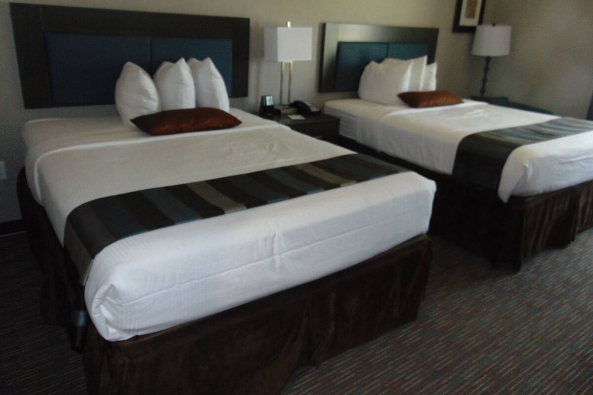 A hotel room with two beds, each with a headboard, bedside tables, lamps, and a carpeted floor.