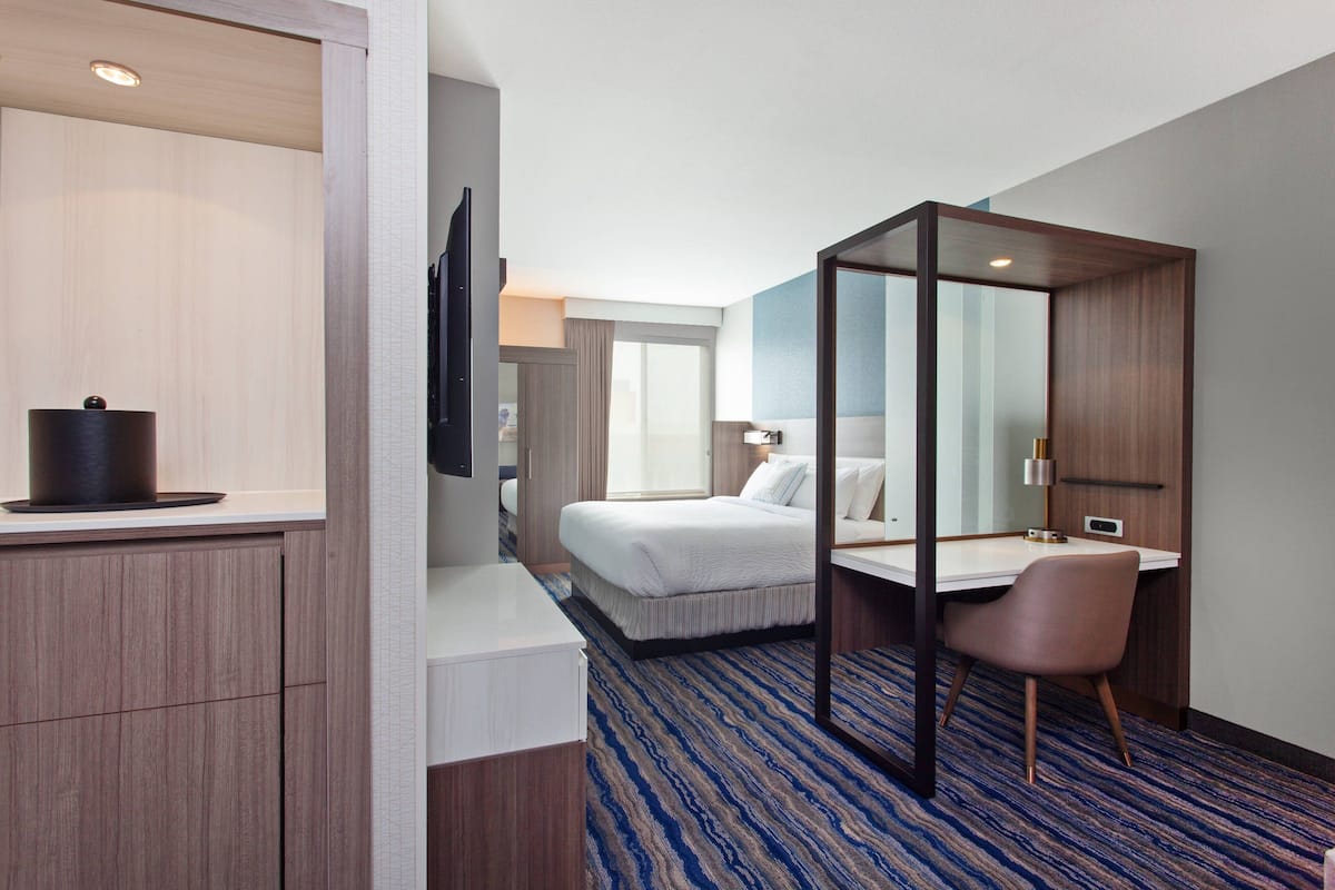 A hotel room with a bed, a desk, a chair, a TV, and a bathroom.
