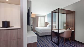 A hotel room with a bed, a desk, a chair, a TV, and a bathroom.