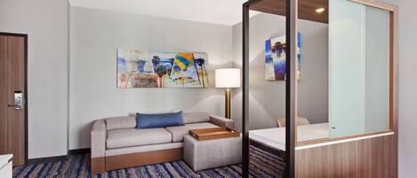 Habitación de hotel con sofá, mesita de noche, lámpara y un espejo grande.