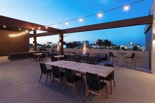 Un patio al aire libre con mesas y sillas, luces colgantes y vistas de la ciudad.