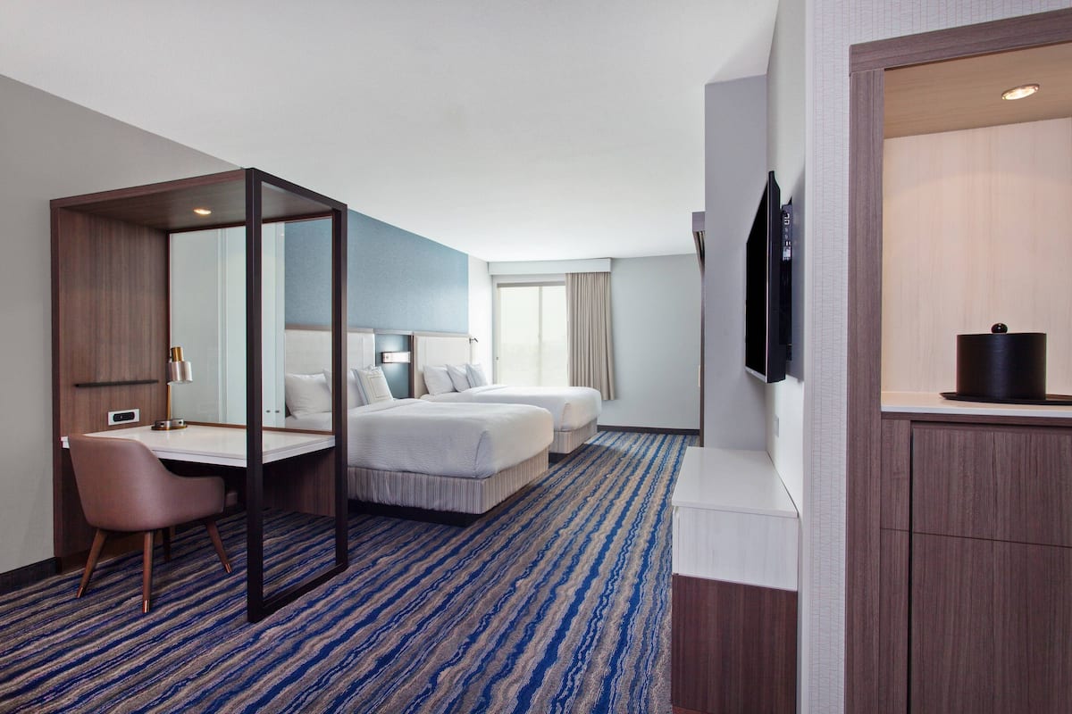A hotel room with a large bed, a desk, a chair, a TV, and a bathroom area.