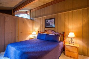 A wooden-paneled bedroom with a bed, two bedside tables with lamps, and a framed picture on the wall. - Elk Lane 10 (Bend)
