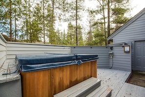 A wooden hot tub on a wooden deck with a view of trees in the background.