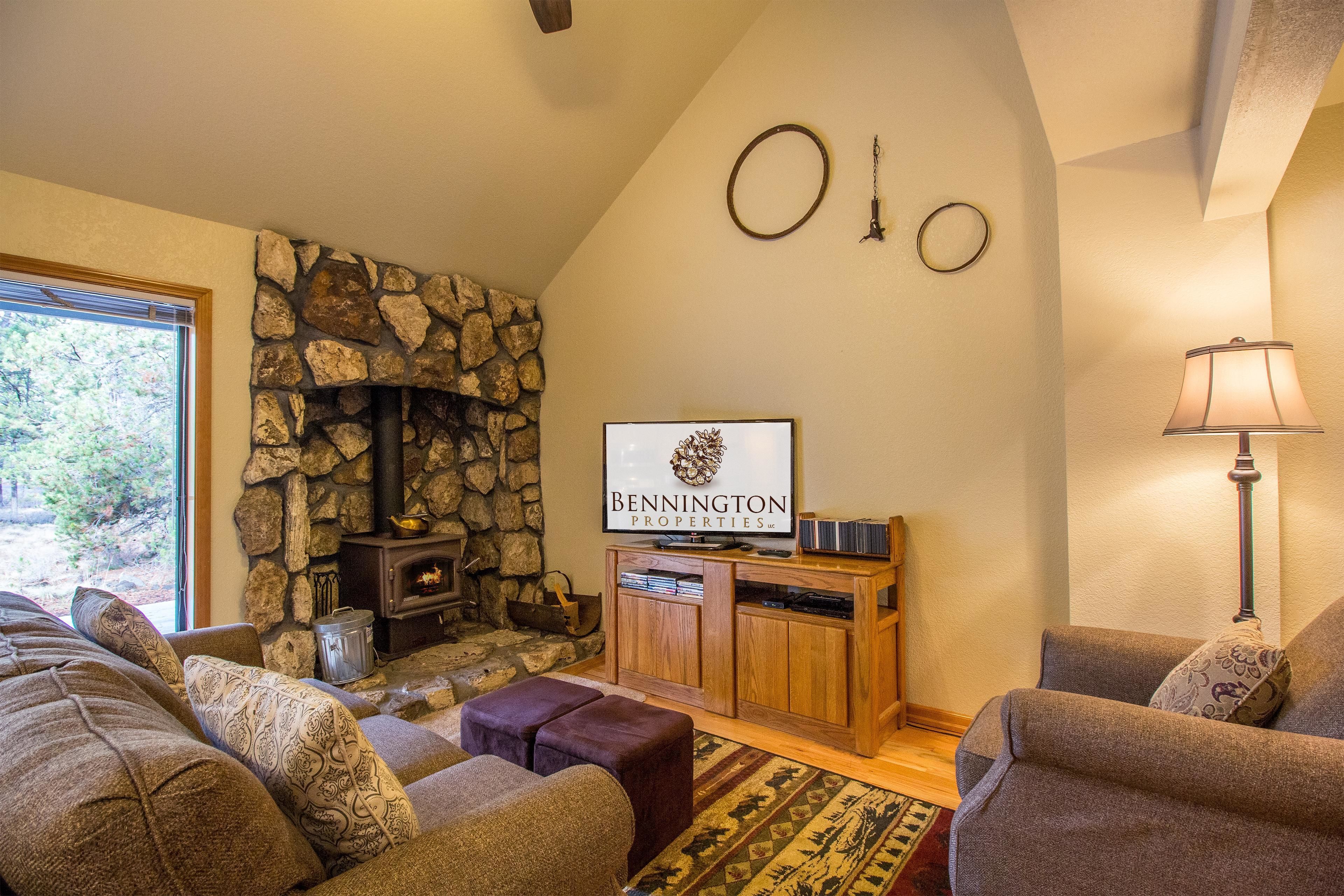 A cozy living room with a stone fireplace, comfortable seating, and a television displaying 'BENNINGTON PROPERTIES'.